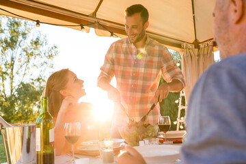 Young man serving salad to wife at sunny patio table