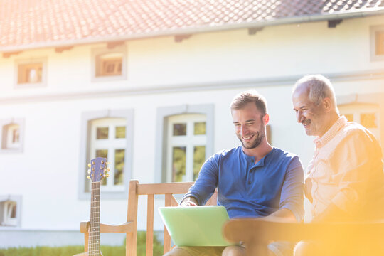 Father and adult son using laptop on garden bench