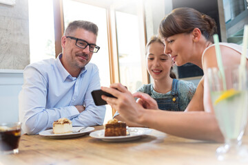 Family with cell phone eating dessert at cafe table