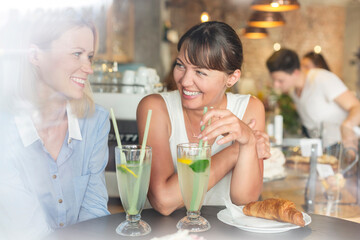 Smiling women drinking lemonade at cafe table