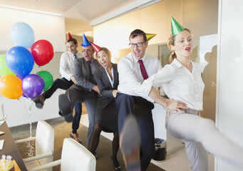 Playful business people with party hats dancing in conga line - obrazy, fototapety, plakaty