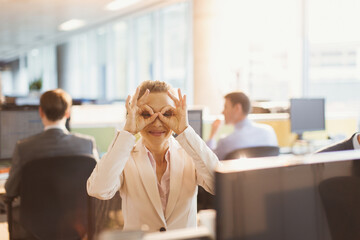 Portrait playful businesswoman pretending to wear glasses at desk in office