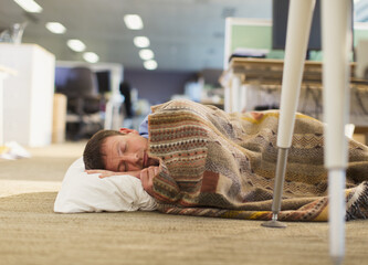Businessman with pillow and blanket sleeping on office floor