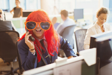 Portrait playful businessman wearing red wig huge sunglasses in office