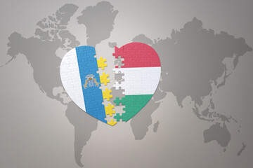 puzzle heart with the national flag of hungary and canary islands on a world map background.Concept.