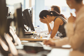 Stressed businesswoman with head in hands at office desk - obrazy, fototapety, plakaty