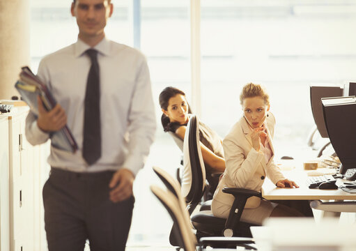 Businesswomen checking out passing businessman in office