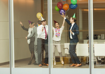 Business people wearing party hats dancing balloons at conference room window