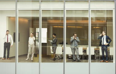 Business people talking on cell phones reviewing paperwork at conference room window