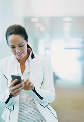 Smiling businesswoman using cell phone in office corridor