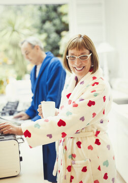 Portrait smiling mature woman drinking coffee in bathrobe at kitchen counter