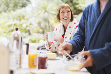 Smiling mature woman drinking coffee in bathrobe at breakfast