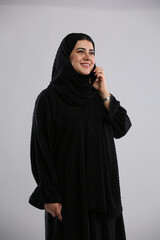 saudi arabian woman in hijaab standing with phone in hand and talking with a smile
