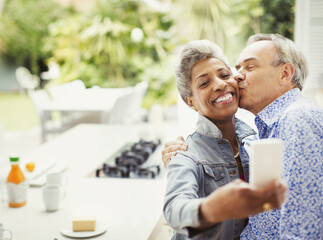 Affectionate mature couple kissing taking selfie in kitchen