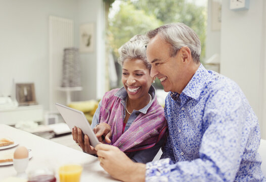 Smiling mature couple sharing digital tablet at breakfast table