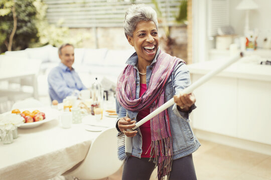 Portrait playful mature woman playing air guitar with stick in kitchen