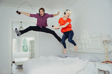 Playful couple jumping on bed listening to music mp3 player headphones - obrazy, fototapety, plakaty