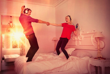 Playful couple dancing on bed listening to music mp3 players headphones