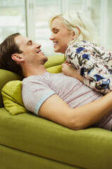 Affectionate couple laying on living room sofa face to face