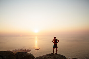 Male runner on rocks looking at sunset ocean view - Powered by Adobe