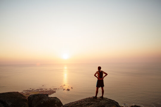 Male runner on rocks looking at sunset ocean view