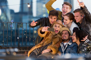 Enthusiastic young adult friends taking selfie at rooftop party