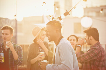 Young man laughing and drinking at rooftop party - Powered by Adobe
