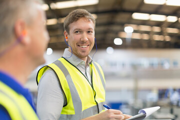 Supervisor with clipboard smiling at worker in steel factory
