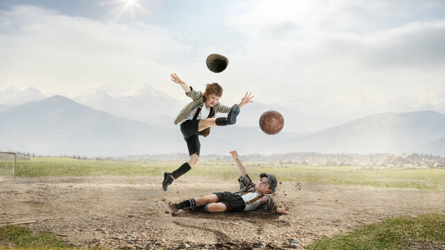 Little boys, children in retro style clothes playing football outdoors on a daytime, falling on dirt, kicking ball in jump