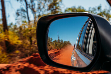 Red clay dust cloud in side-view mirror of car