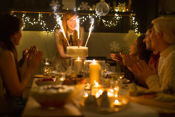 Woman serving Christmas cake sparkler fireworks to clapping family