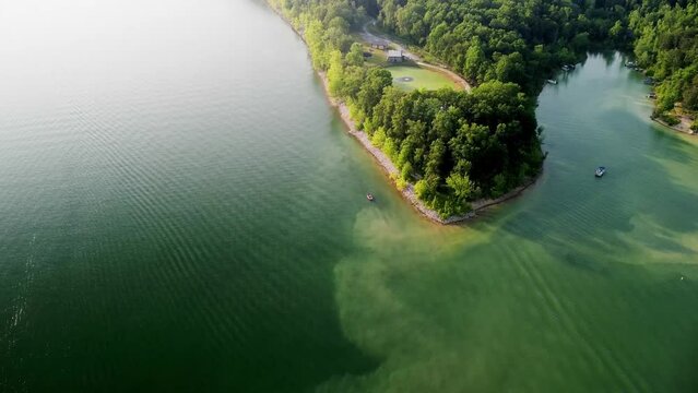 Different shades of emerald colored waters of Cave Run lake in Kentucky. Forest and vacation home buildings on the coastline. Recreational boats sailing on the lake surface.