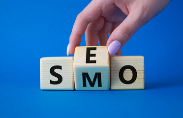 SEO vs SMO symbol. Businessman hand turns wooden cubes and changes the word SMO to SEO. Beautiful blue background. SEO vs SMO and business concept. Copy space