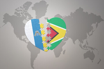 puzzle heart with the national flag of guyana and canary islands on a world map background.Concept.