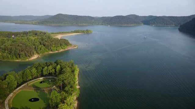 During a sunny evening in northeast Kentucky, a still perspective of Cave Run Lake and Daniel Boone National Forest. The water's surface displayed gentle waves and boats are gliding across it.