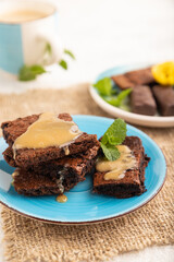 Chocolate brownie with caramel sauce with a cup of coffee on gray concrete, side view, selective focus.