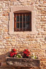 front view, medium distance of, a bared window in a limestone, brick wall and a cut stone planter with flowers