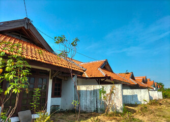 One of the houses in Indonesia near the road in a village. White house under the tropical blue sky on a sunny day. White house with traditional clay made tile roof. Close-up.

