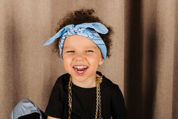 Portrait of a Cool Cute little girl laughing and smiling, wearing gold chains, brown background