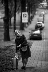 A woman with a suitcase is standing on the street. Black and white photo.
