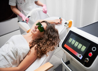 Joyful curly woman with glasses, who is in session of laser hair removal in axillary area of body. Modern, pleasant and painless method of losing unwanted hair.