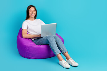 Photo of pretty young girl hold computer smile sit bean chair isolated over blue color background