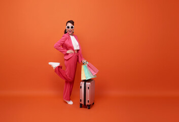 Full-length of happy smiling woman tourist carrying shopping bags and suitcase for summer sale shopping isolated on orange background.