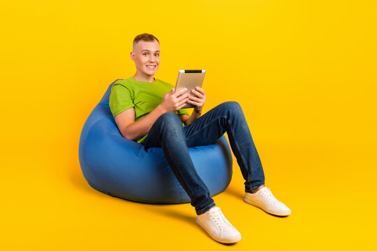 Full Body Profile Photo Of Positive Person Sitting Big Soft Chair Use Tablet Isolated Yellow Color Background