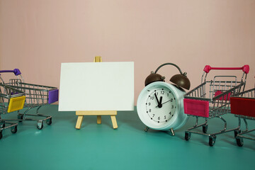 Card mockup space for copy text message on easel standing with alarm clock on pink and blue background