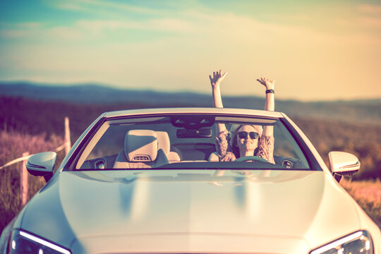 Happiness in a convertible. Young woman full of success with arms raised. Sunset.