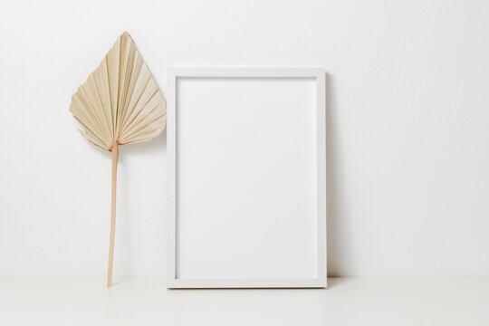 Wooden mockup photo frame with palm leaf on white table. Photo  frame for design and poster, aesthetic home decoration, scandinavian style