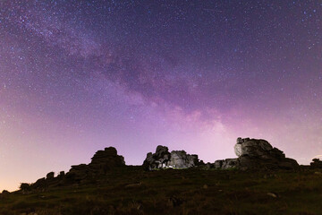 A star filled night sky over a light painted rocky landscape in Dartmoor National Park, UK