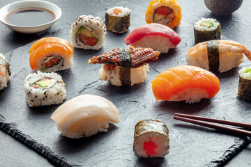 Sushi with chopsticks. Rolls, maki, nigiri on a black background, Japanese food. Salmon, tuna, eel, shrimp and other seafood with rice on a plate at an Asian restaurant