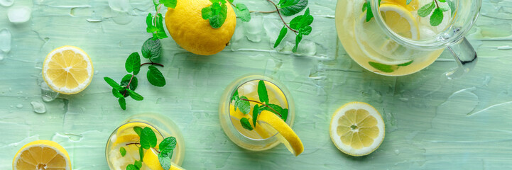 Lemonade with mint panoramic banner. Lemon water drink with ice. Two glasses and a pitcher on a...